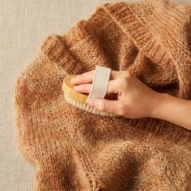 Käsi harjaa ruskeaa villaneuletta vaateharjalla